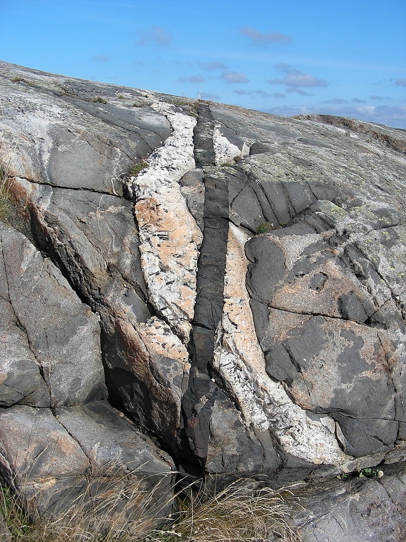 A light gray igneous rock cross-cuts in a younger white pegmatite dike, cross-cut by an even younger black diabase dike